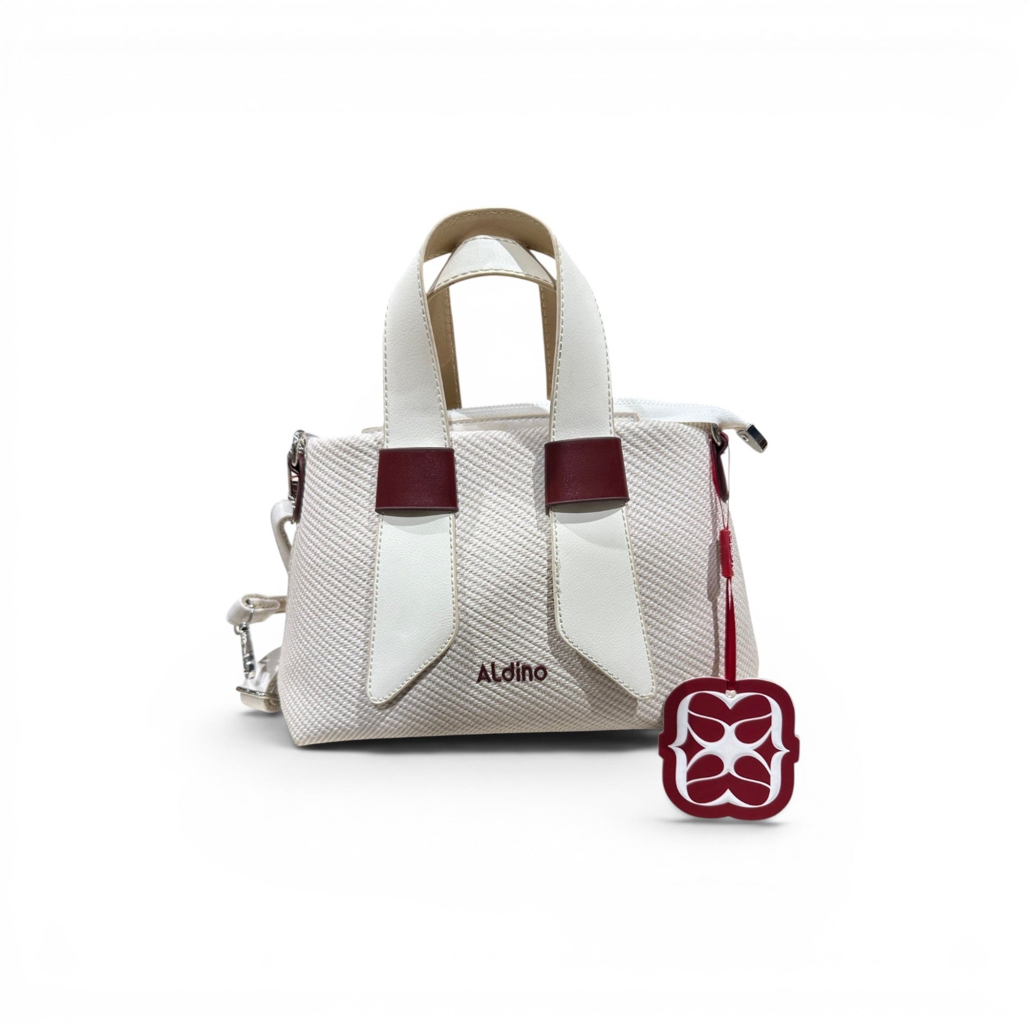 COC Store Aldino textured top handle bag in off-white fabric with white and burgundy faux leather accents and a decorative charm.